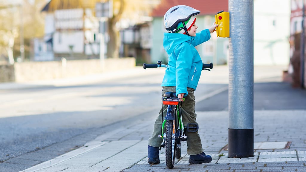 A child stops at a traffic light and pushes the button to ask for green light. 